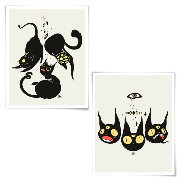 Two framed art prints featuring surreal black cat illustrations on a light cream background. The left print shows two black cats with yellow eyes and small red accents, and the right print shows three expressive black cat faces with yellow eyes and a small red eye above them.