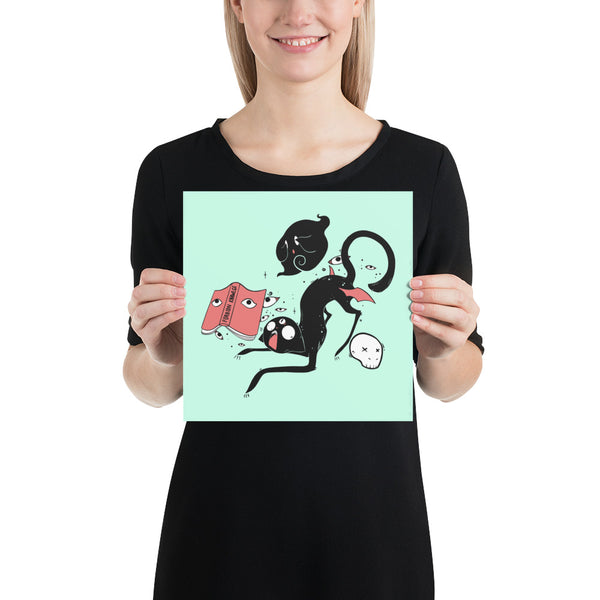 Woman holding a matte art print of Kuro, the black cat, with playful characters on a mint green background.