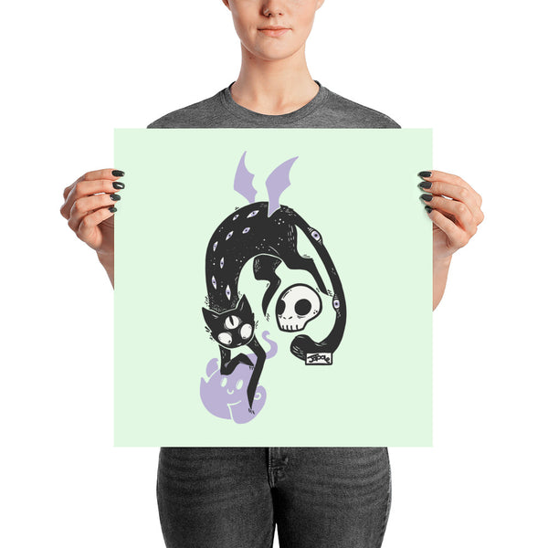 Kuro black cat art print poster with a skull and ghost friend, held by a person on mint green background.