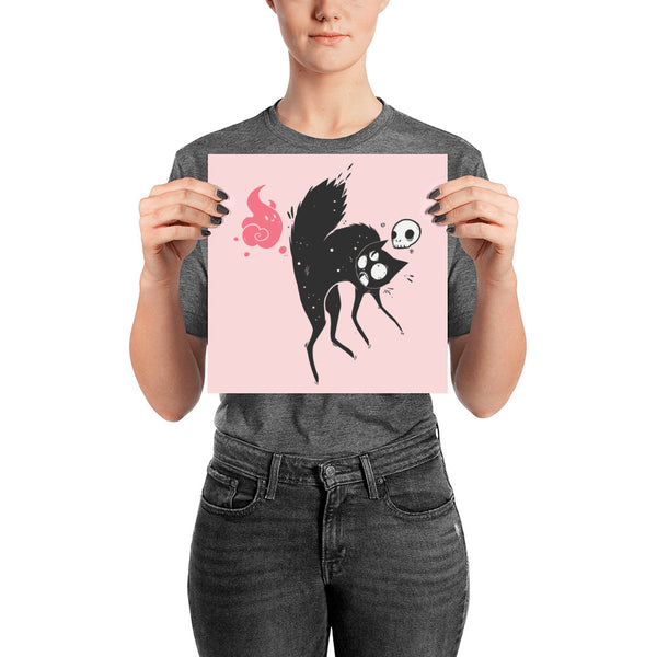 Person holding a Kuro black cat art print poster featuring a cat with a skull and ghost on a pink background.