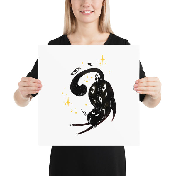 Woman holding a matte art print of a stretching black cat surrounded by stars and eyes, showcasing original illustration.