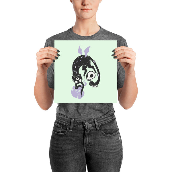 Kuro Black Cat Matte Art Print featuring a black cat, skull, and ghost on pastel background, held by a person.