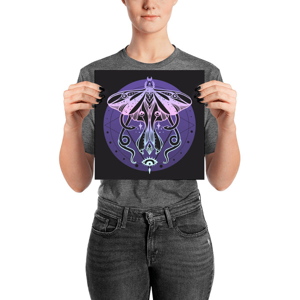 Woman holding a matte art print of a luna moth and snakes illustration on a black background.