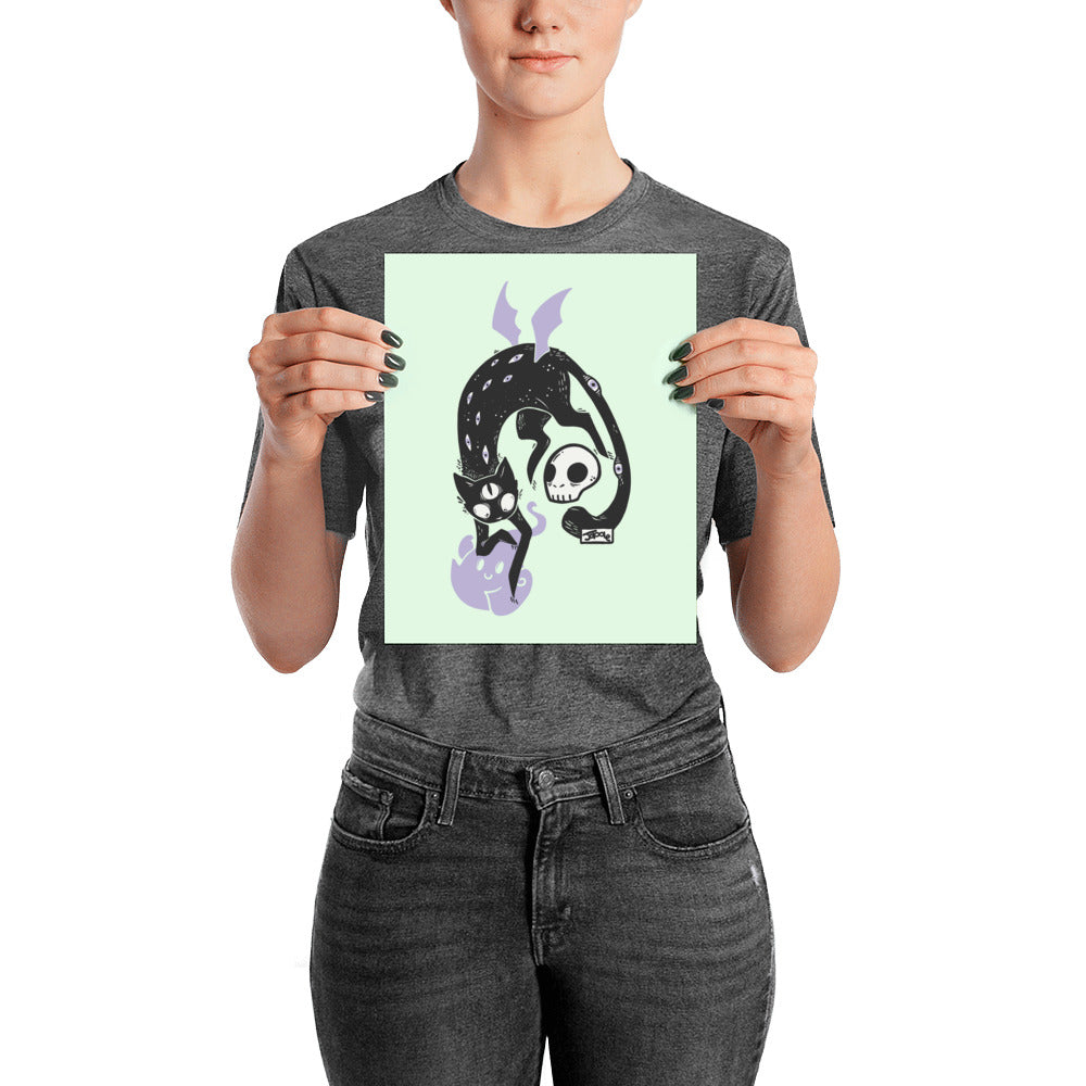 Matte art print of a black cat Kuro with a skull and ghost, held by a person against a mint background.