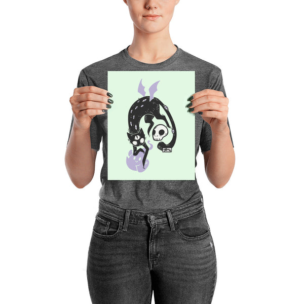 Matte art print of a black cat Kuro with a skull and ghost, held by a person against a mint background.